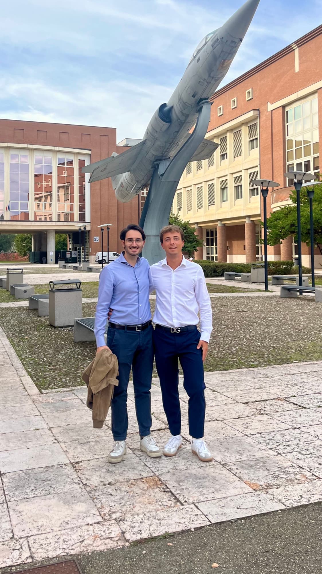 Due ragazzi in piedi davanti a un monumento con un aereo da caccia, in un campus