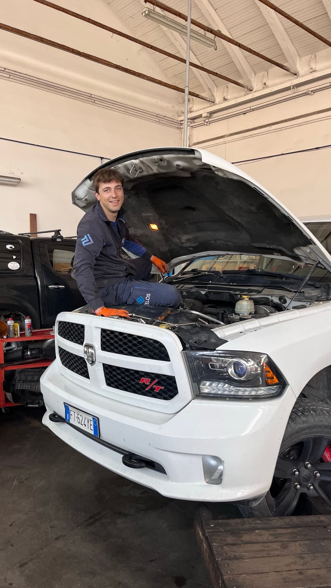 Nicolò Bianchi in officina, seduto sul frontale di un pick-up con il cofano aperto